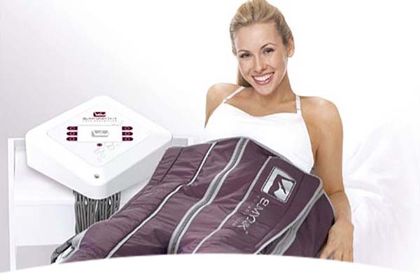 Lächende Frau liegt mit einer Airmax-Kompressionsmanschette an den Beinen entspannt auf einem Bett.