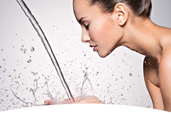 Frau beugt sich vor, hält ihre Hände unter einen Wasserstrahl und spritzt Wasser ins Gesicht.